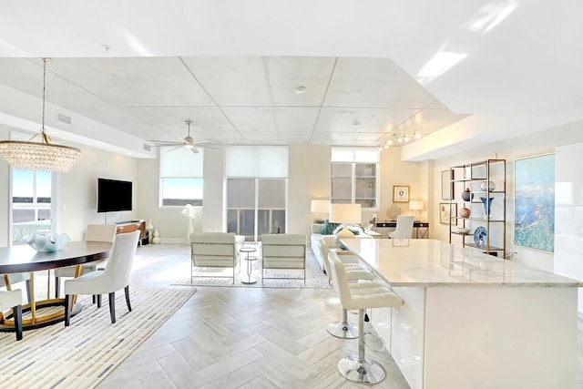 kitchen featuring ceiling fan with notable chandelier, hanging light fixtures, light stone countertops, a breakfast bar area, and light parquet flooring