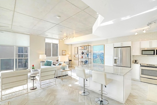 kitchen with white cabinetry, tasteful backsplash, light stone counters, a breakfast bar, and appliances with stainless steel finishes