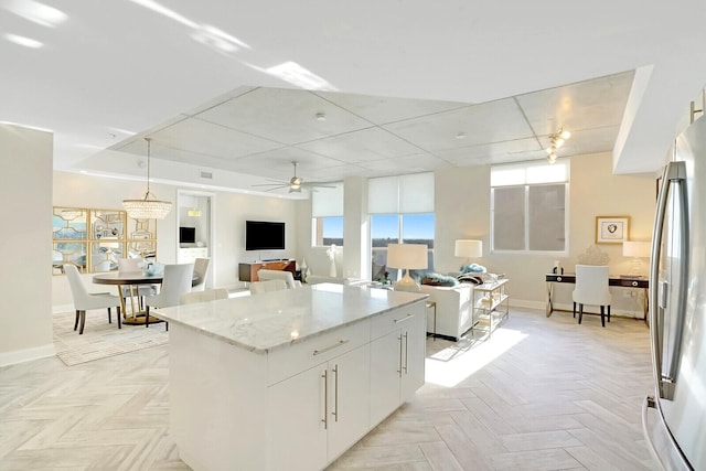 kitchen with pendant lighting, white cabinets, ceiling fan, stainless steel fridge, and a kitchen island