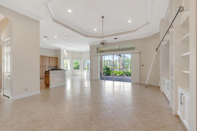 unfurnished living room with a raised ceiling, ceiling fan, crown molding, and light tile patterned floors