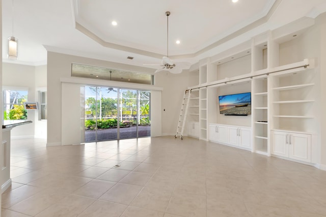 unfurnished living room with ceiling fan, a high ceiling, built in features, a tray ceiling, and ornamental molding