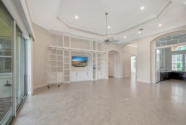 unfurnished living room with a raised ceiling, ceiling fan, built in features, ornamental molding, and light tile patterned floors