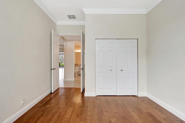 unfurnished bedroom with hardwood / wood-style flooring, crown molding, and a closet