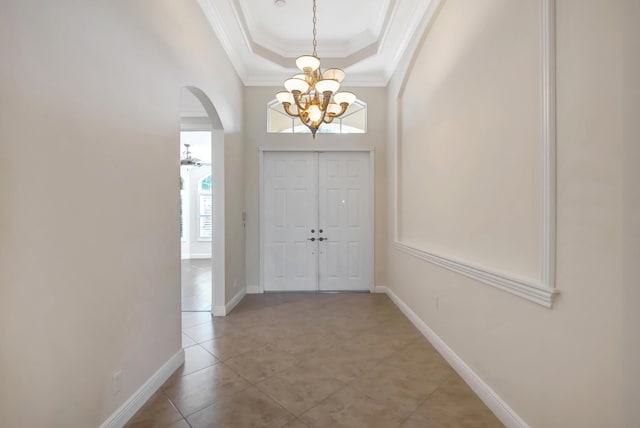 tiled foyer entrance with a notable chandelier, a raised ceiling, ornamental molding, and a towering ceiling