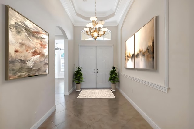 entryway with a high ceiling, a raised ceiling, ornamental molding, and a notable chandelier