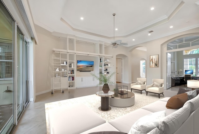 living room featuring built in shelves, a tray ceiling, ceiling fan, and crown molding