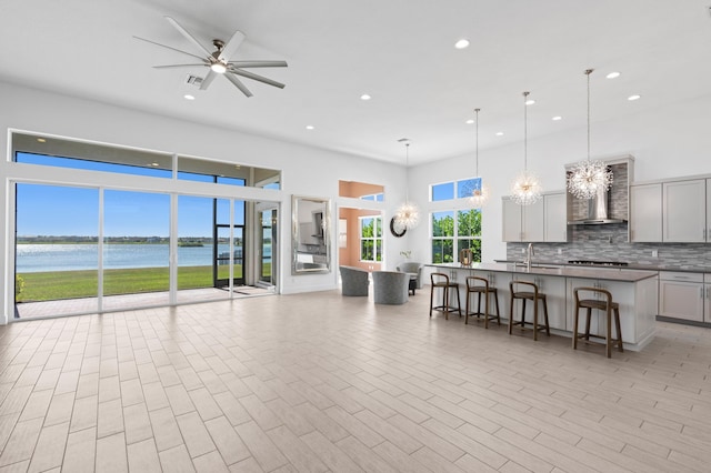 kitchen featuring wall chimney exhaust hood, hanging light fixtures, an island with sink, a kitchen breakfast bar, and a water view