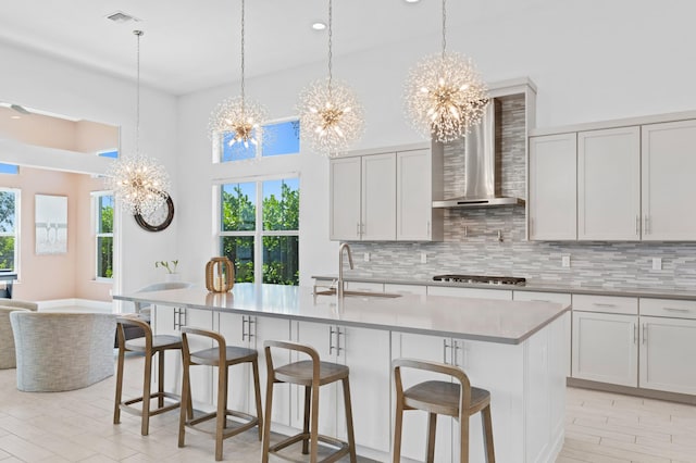 kitchen with a center island with sink, wall chimney range hood, tasteful backsplash, and sink