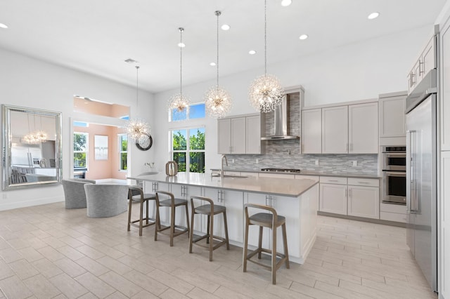 kitchen featuring sink, stainless steel appliances, an inviting chandelier, wall chimney exhaust hood, and pendant lighting