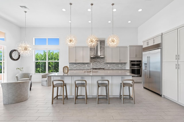 kitchen featuring a chandelier, stainless steel appliances, hanging light fixtures, wall chimney range hood, and tasteful backsplash