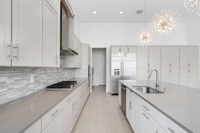 kitchen with sink, stainless steel appliances, decorative light fixtures, wall chimney exhaust hood, and a chandelier