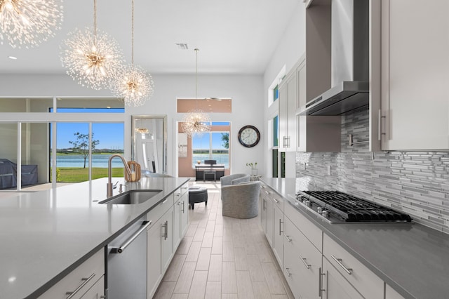 kitchen with a water view, wall chimney range hood, a chandelier, and sink