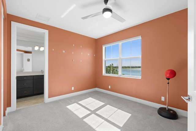 unfurnished bedroom with ceiling fan, ensuite bathroom, light carpet, and a water view