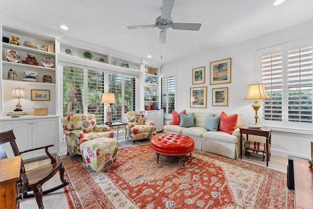 living room with built in shelves, ceiling fan, and light wood-type flooring