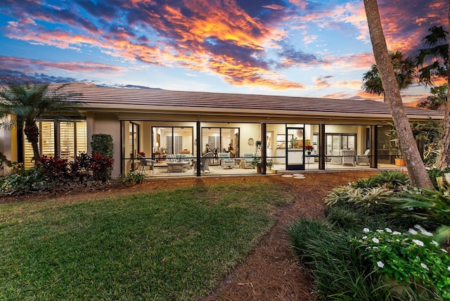 back house at dusk featuring a lawn