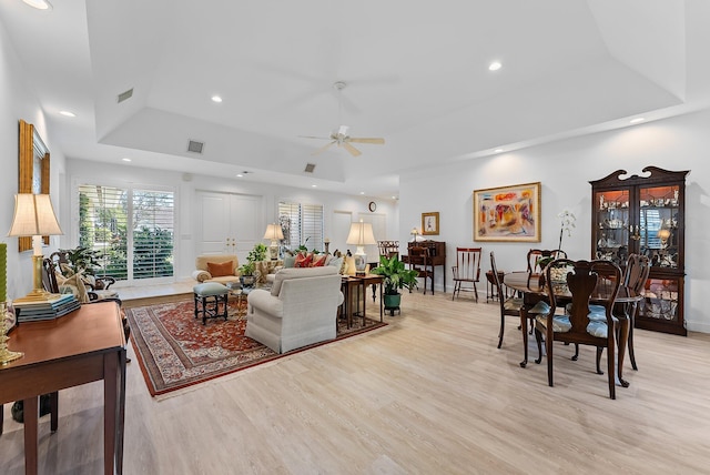 living room with ceiling fan, a raised ceiling, and light wood-type flooring