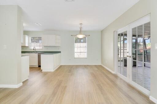 interior space with white cabinets, decorative light fixtures, light hardwood / wood-style flooring, and plenty of natural light