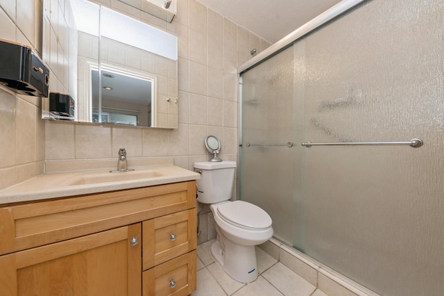 bathroom featuring toilet, a shower with shower door, tile walls, vanity, and tile patterned flooring