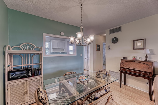 kitchen with decorative light fixtures, an inviting chandelier, a textured ceiling, and light hardwood / wood-style flooring