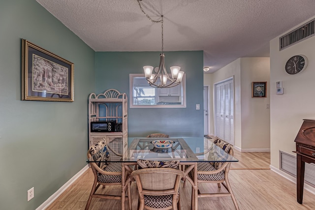 dining space with a notable chandelier, a textured ceiling, and light wood-type flooring