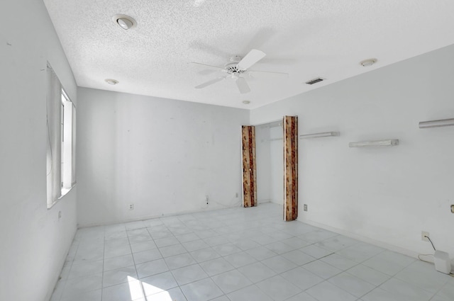 empty room featuring ceiling fan, light tile patterned floors, and a textured ceiling