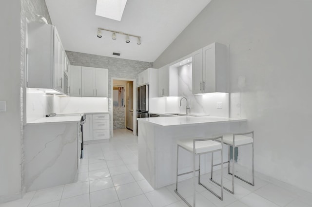 kitchen with sink, lofted ceiling with skylight, white cabinets, decorative backsplash, and kitchen peninsula