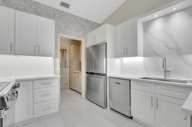 kitchen featuring white cabinetry, sink, stainless steel appliances, light tile patterned floors, and tile walls