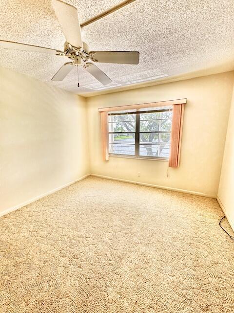 carpeted empty room with ceiling fan and a textured ceiling