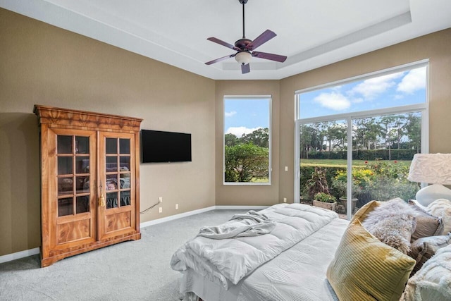 bedroom with carpet flooring, ceiling fan, a tray ceiling, and multiple windows