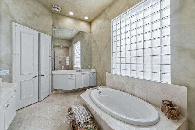 bathroom with tile patterned flooring, vanity, and a relaxing tiled tub