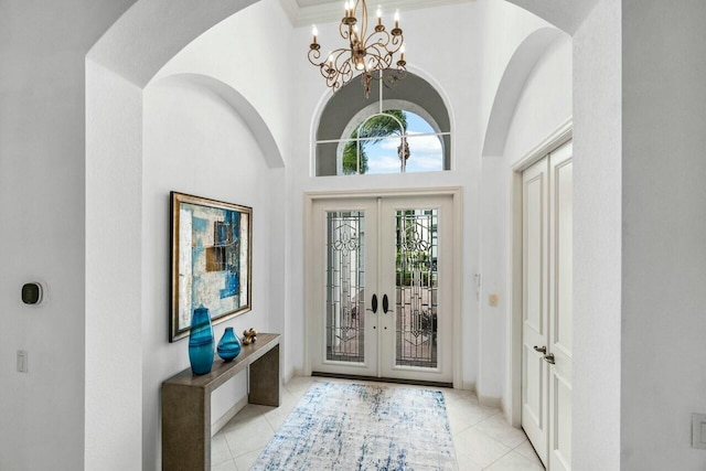 tiled entryway with french doors, ornamental molding, a notable chandelier, and a high ceiling