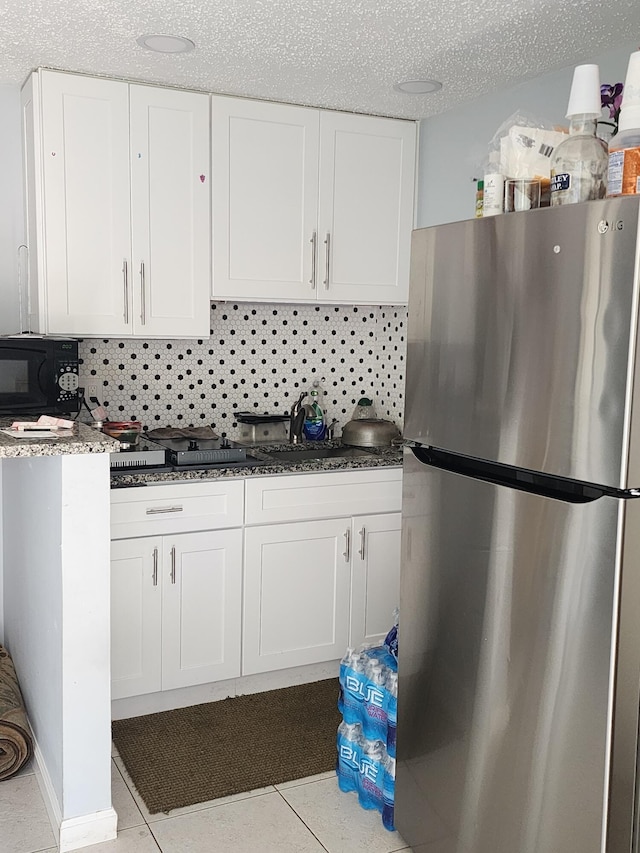 kitchen featuring white cabinetry, backsplash, and stainless steel refrigerator