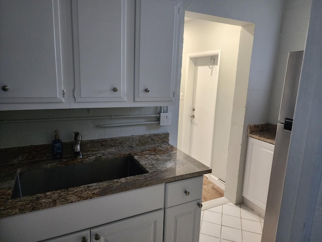 kitchen with white cabinetry, sink, light tile patterned flooring, and dark stone counters