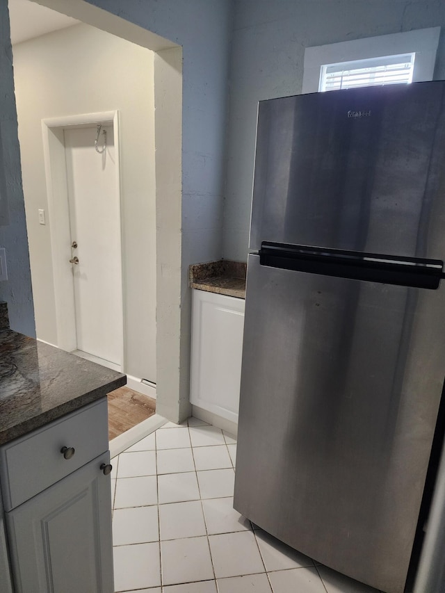 kitchen with stainless steel refrigerator, dark stone countertops, white cabinets, and light tile patterned floors