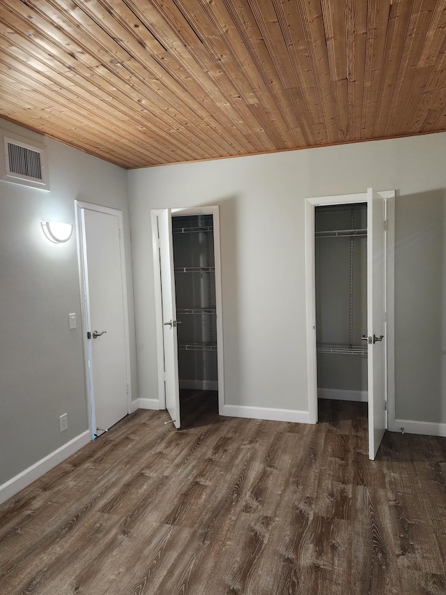 unfurnished bedroom with dark wood-type flooring, wooden ceiling, and two closets