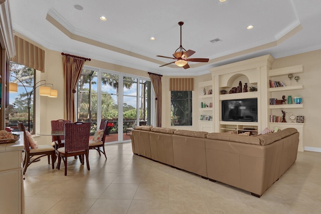 tiled living room featuring built in shelves, a tray ceiling, ceiling fan, and crown molding