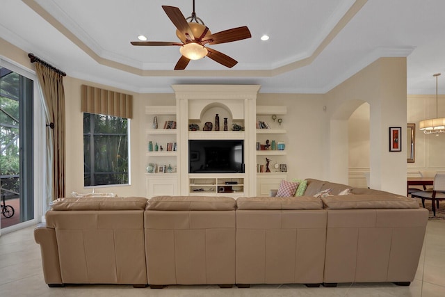 living room featuring ceiling fan with notable chandelier, light tile patterned flooring, ornamental molding, and a tray ceiling