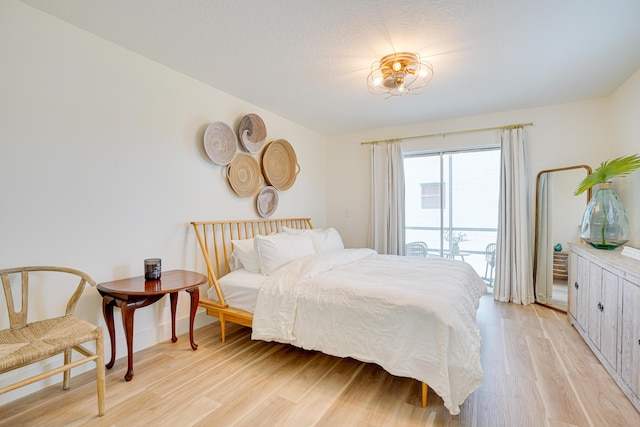 bedroom with access to exterior, light wood-type flooring, and a textured ceiling