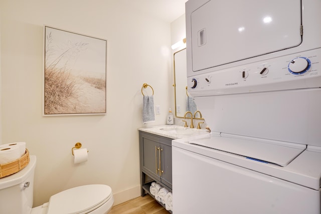 bathroom featuring vanity, stacked washing maching and dryer, toilet, and hardwood / wood-style flooring