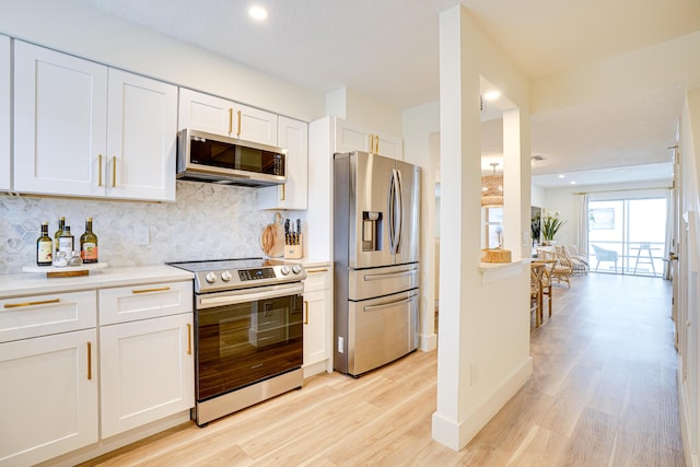 kitchen with backsplash, white cabinetry, stainless steel appliances, and light hardwood / wood-style floors