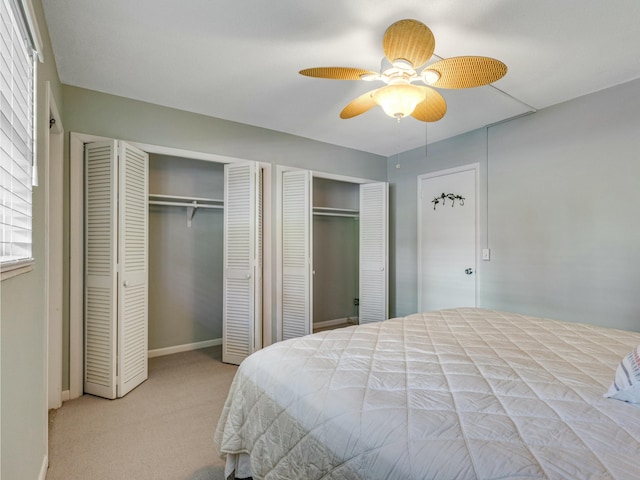 bedroom with ceiling fan, light carpet, and two closets