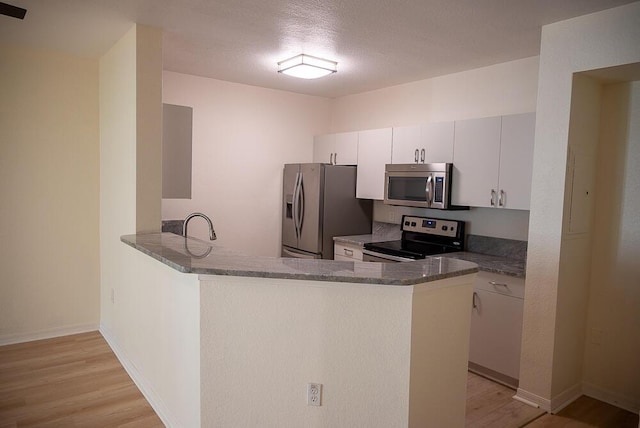 kitchen featuring white cabinets, light hardwood / wood-style flooring, dark stone countertops, kitchen peninsula, and stainless steel appliances