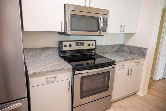 kitchen with light stone counters, stainless steel appliances, white cabinets, and light wood-type flooring