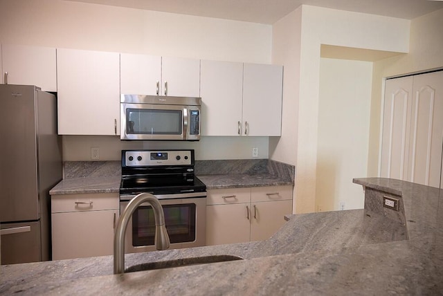 kitchen with white cabinetry, appliances with stainless steel finishes, sink, and dark stone countertops