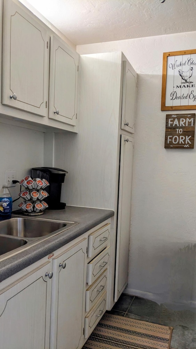 kitchen with dark tile patterned flooring, dark countertops, and a sink