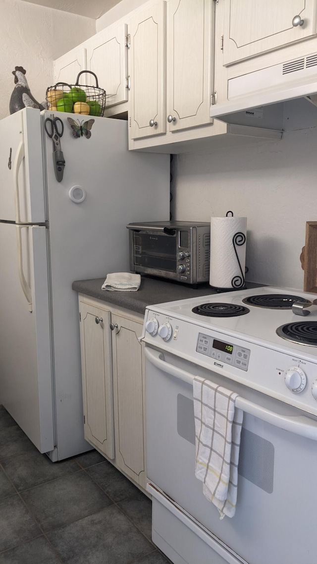 kitchen with a toaster, white appliances, dark tile patterned floors, and under cabinet range hood