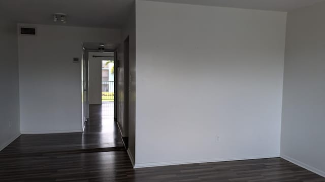 unfurnished room with dark wood-style flooring, visible vents, and baseboards