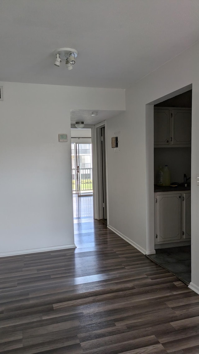 empty room featuring dark wood-type flooring, visible vents, and baseboards