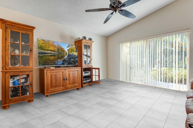 living room with ceiling fan, light tile patterned floors, a textured ceiling, and vaulted ceiling