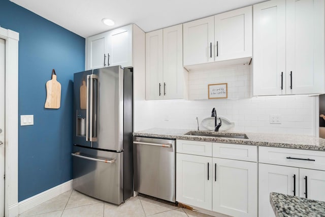 kitchen featuring white cabinets, sink, light stone countertops, light tile patterned floors, and appliances with stainless steel finishes